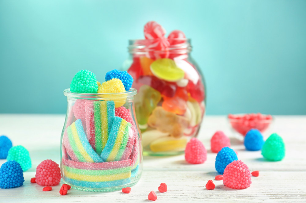 Glassware,With,Different,Chewy,Candies,On,Table,Against,Color,Background