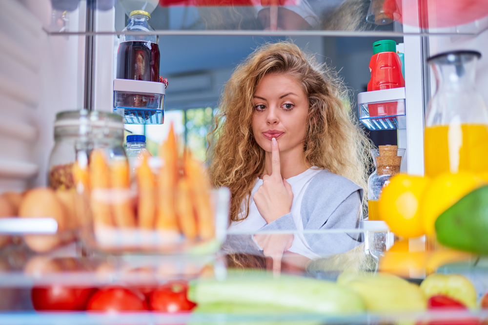Confused,Hungry,Woman,Holding,Finger,On,Mouth,While,Standing,In