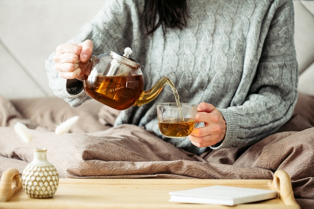 Woman,Dressed,In,Knitted,Sweater,Pours,Hot,Tea,From,Glass